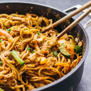 stirring peanut noodles in a black pan