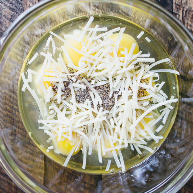 Raw eggs and shredded cheese in a glass bowl