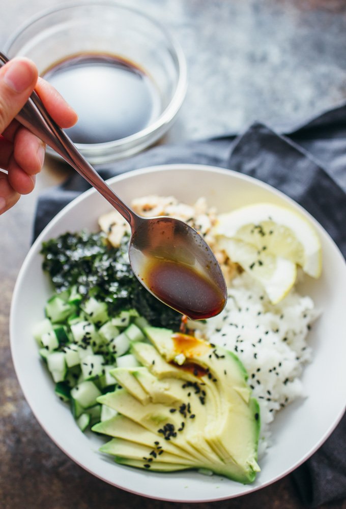 spooning dressing over salmon roll sushi bowl