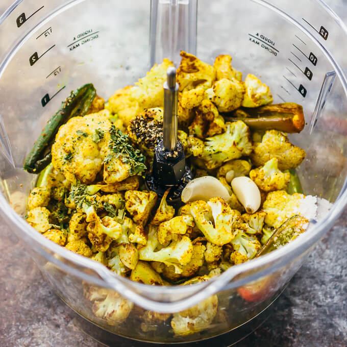 A food processor bowl with curried cauliflower, jalapeno, and garlic to make a dip