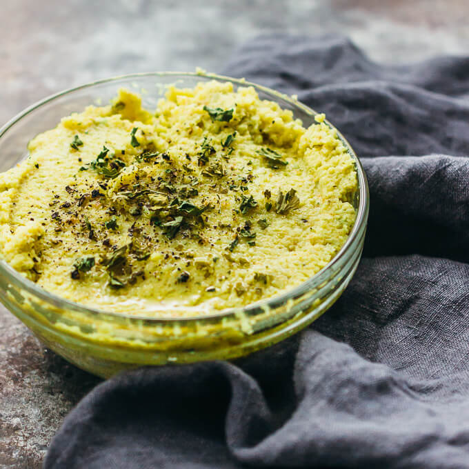 Roasted curry cauliflower dip served in a glass bowl and topped with herbs and pepper