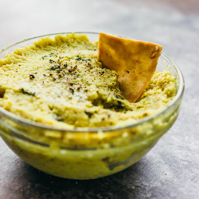Roasted curry cauliflower dip in a glass bowl with pita chip