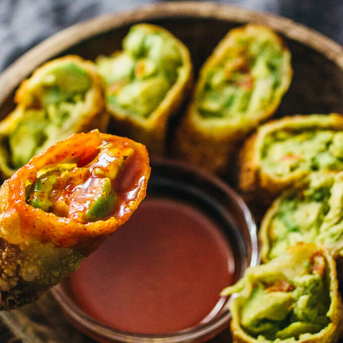 lifting up an avocado egg roll with sauce