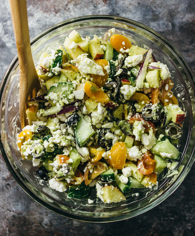 stirring greek salad with avocado dressing