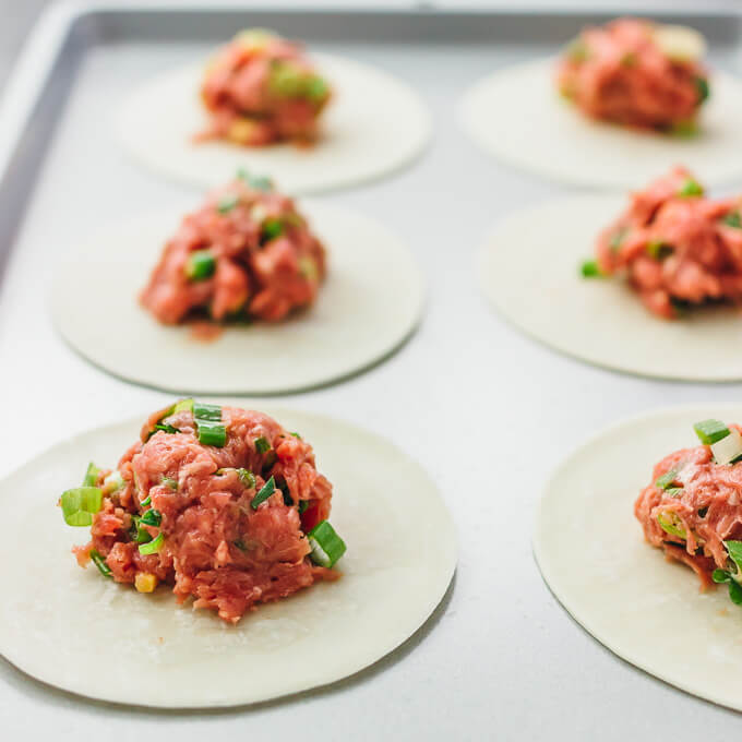 assembling dumpling filling with ground beef and sliced scallions on wrappers