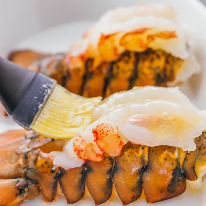 brushing lemon garlic butter over lobster tails