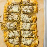 Make this healthy, low carb flatbread recipe using riced cauliflower. It's topped with pesto sauce and grated parmesan cheese.