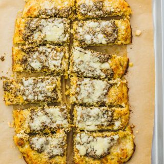 Make this healthy, low carb flatbread recipe using riced cauliflower. It's topped with pesto sauce and grated parmesan cheese.