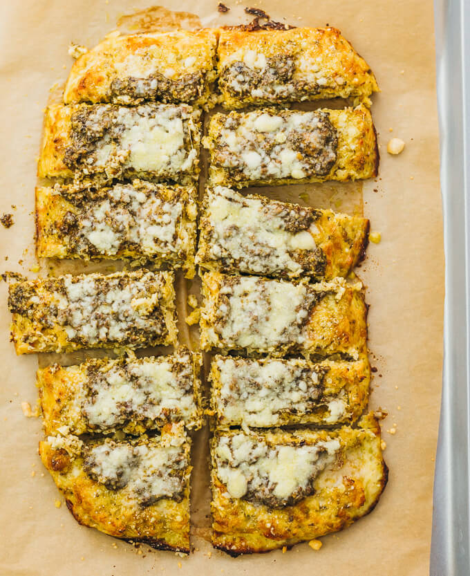 Make this healthy, low carb flatbread recipe using riced cauliflower. It's topped with pesto sauce and grated parmesan cheese.