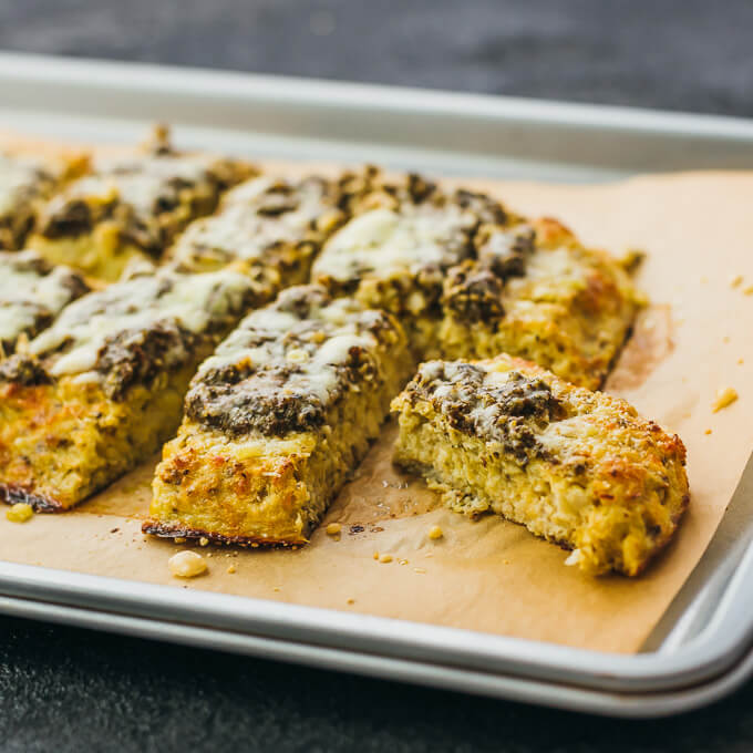 Make this healthy, low carb flatbread recipe using riced cauliflower. It's topped with pesto sauce and grated parmesan cheese.