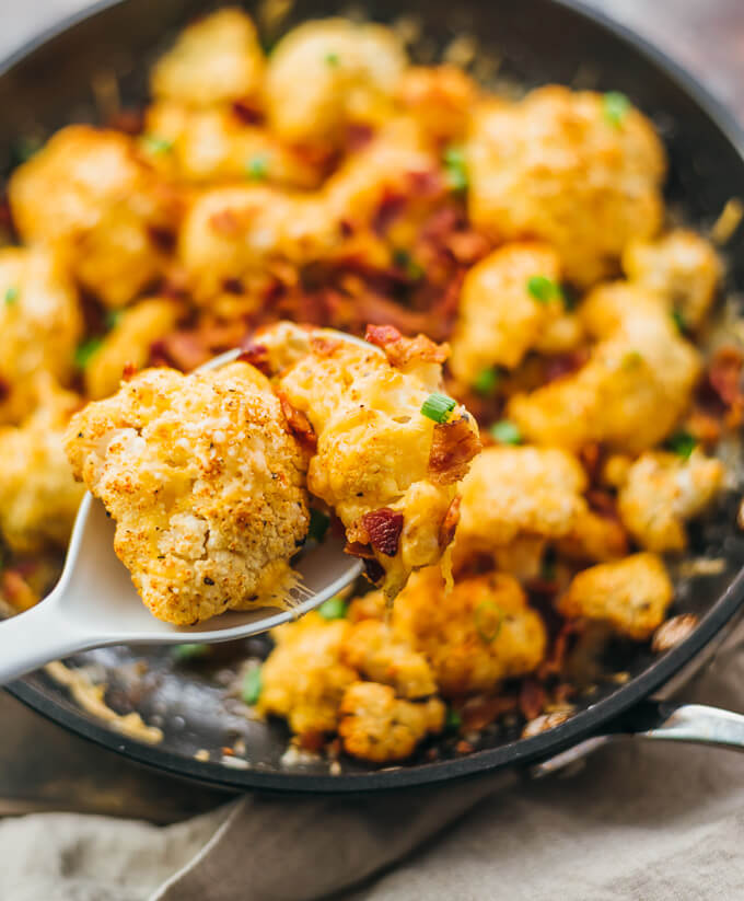 Serving roasted cauliflower loaded with cheddar cheese, bacon, and scallions