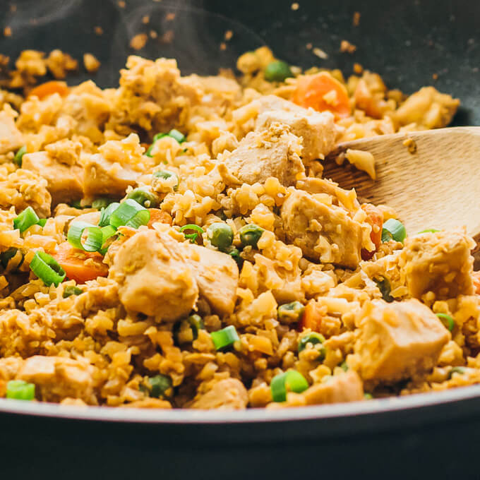 Try this easy cauliflower rice stir fry with chicken and scrambled eggs. Low carb and keto friendly. Cooked in a pan over stovetop, close up view.