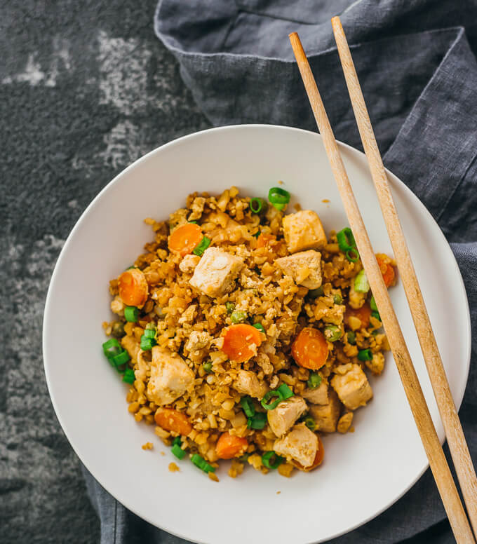 Try this easy cauliflower rice stir fry with chicken and scrambled eggs. Low carb and keto friendly. Served in a plate with chopsticks.