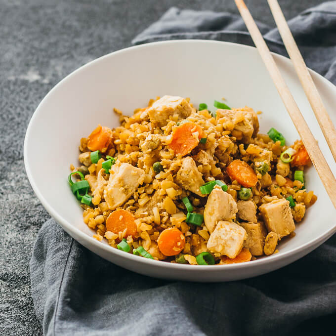 Try this easy cauliflower rice stir fry with chicken and scrambled eggs. Low carb and keto friendly. Served in plate with chopsticks.