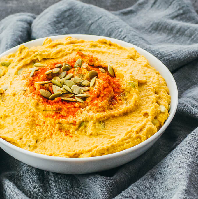Pumpkin hummus in a white bowl and topped with paprika and pumpkin seeds