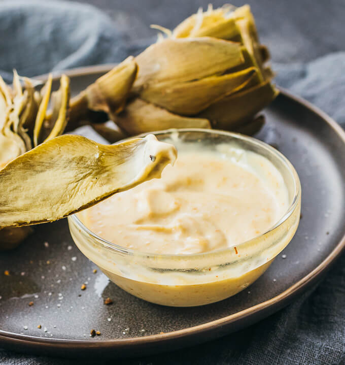 lifting up artichoke leaf with dip on it