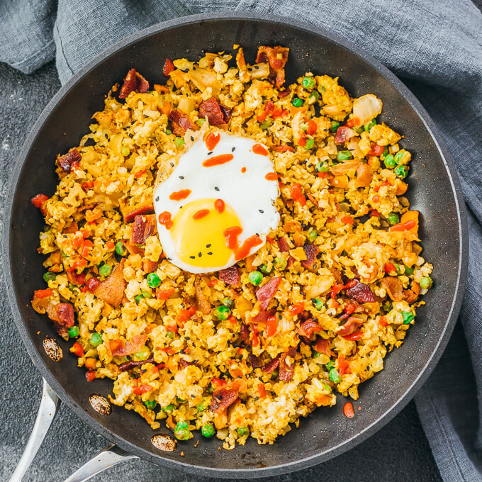 Easy and simple cauliflower fried rice stir fry with egg, bacon, and kimchi in a black pan