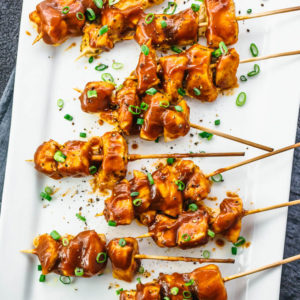 overhead view of chicken satay skewers on white plate