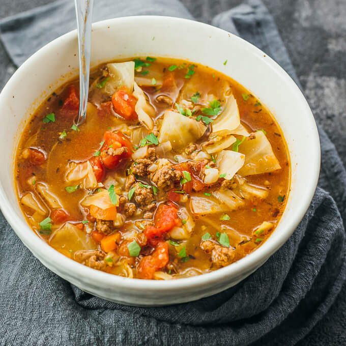 Using a spoon to eat low carb unstuffed cabbage roll soup from a white bowl