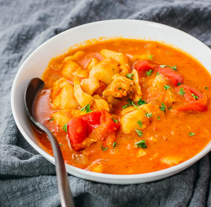 fish stew served in white bowl with black spoon