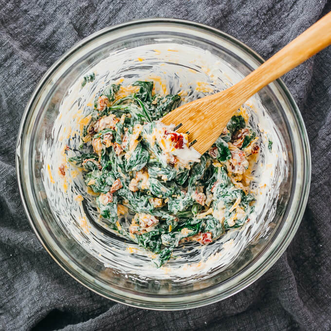 stirring cheesy spinach tomato topping