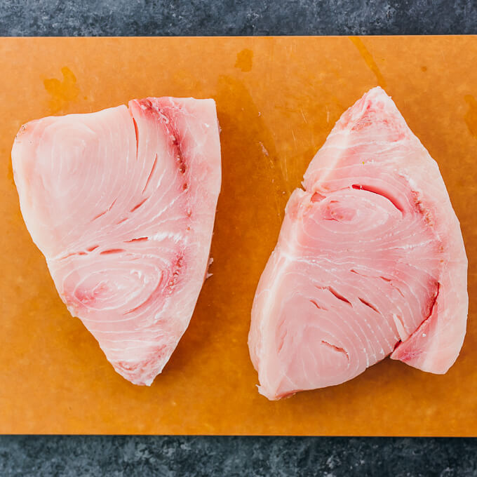 two raw swordfish steaks on a cutting board