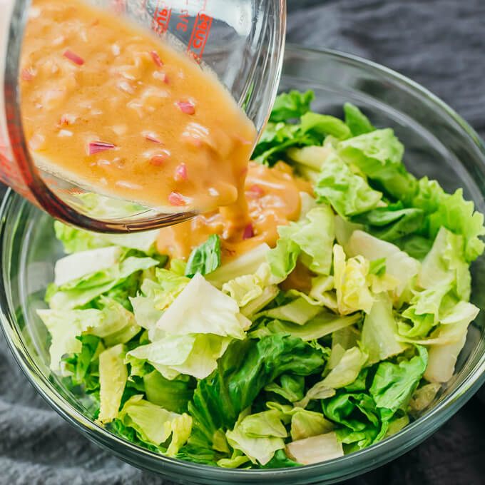 pouring vinaigrette dressing over romaine lettuce