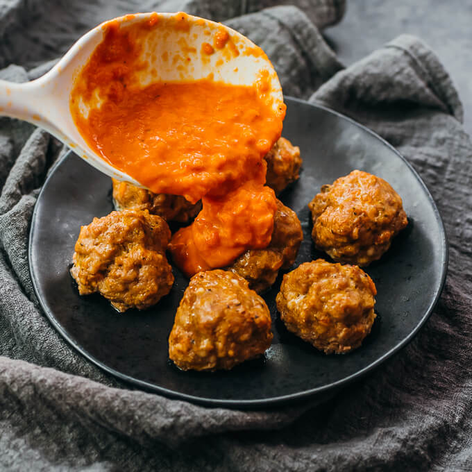 pouring marinara sauce over meatballs