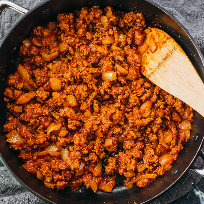 stirring tomato meat sauce in black skillet