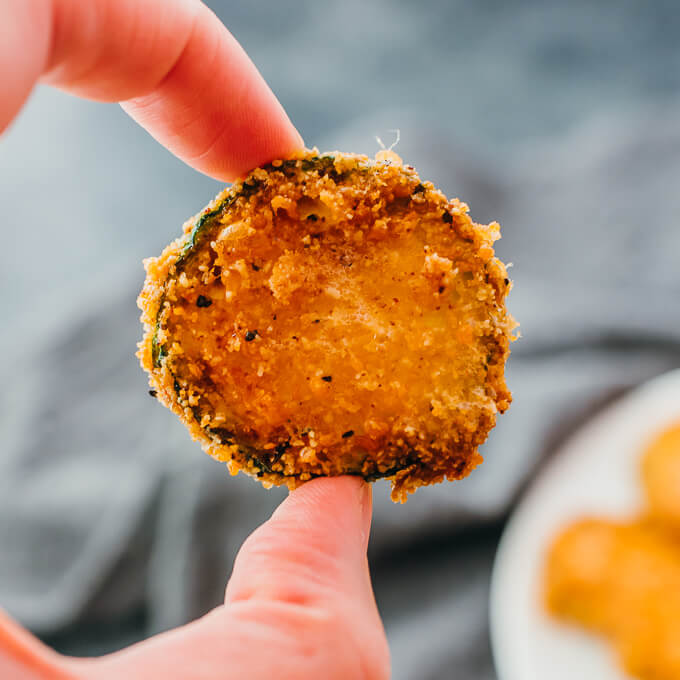 holding up fried zucchini slice using fingers