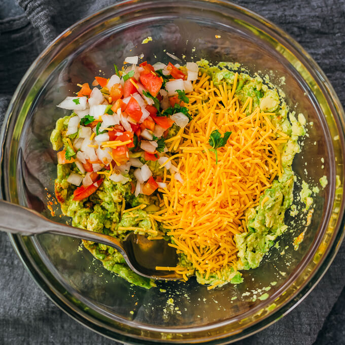 adding cheese and pico de gallo to guacamole