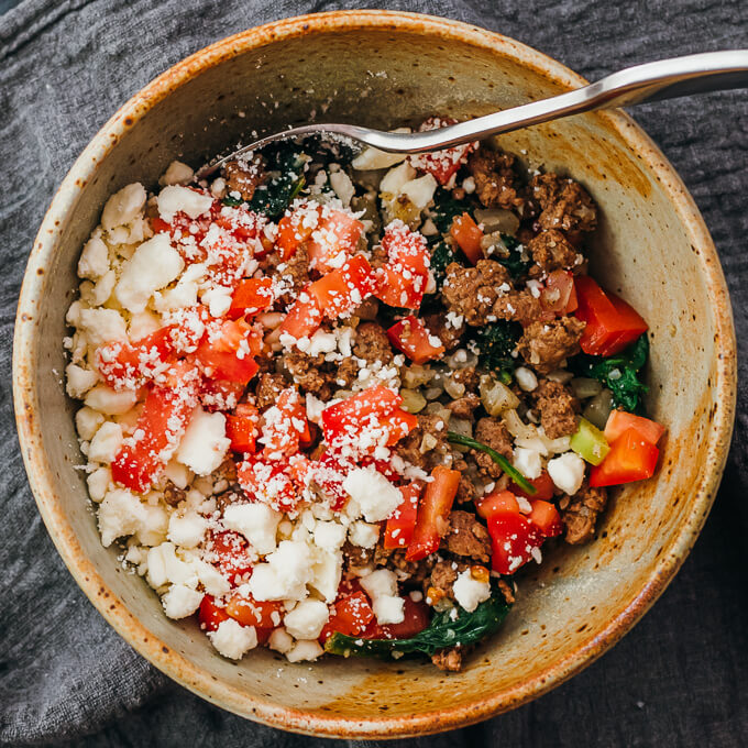 adding feta cheese and tomatoes to ground lamb bowl