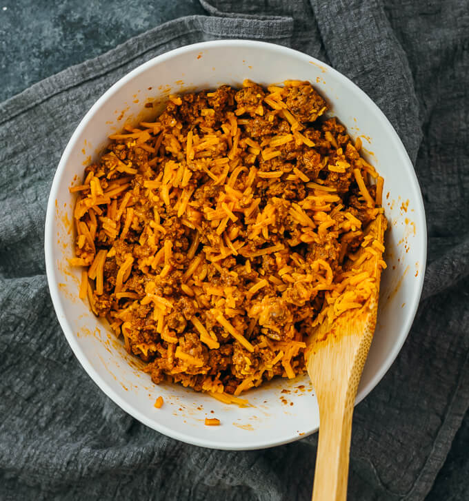 stirring beef mixture with shredded cheddar cheese